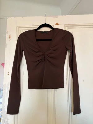 Brun långärmad topp - Jättefin brun långärmad topp från BikBok. Toppen har en v-ringning med en fin detalj framtill. Storlek XS. Den är använd en gång, mycket bra skick! Kontakta om du har frågor💗