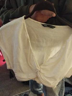 Vit omlottopp från Zara - Vit croppad omlottopp från Zara med korta ärmar och twistad detalj framtill. Djup v-ringning och mjukt, lätt material som passar perfekt till jeans eller kjol.