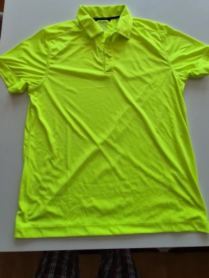 Neongul sportpiké med krage(golf) - Snygg neongul pikétröja i sportigt material med korta ärmar och klassisk krage. Perfekt för träning eller aktiviteter där du vill synas. Tröjan har en enkel design utan tryck eller logga och är tillverkad i ett lätt och snabbtorkande tyg.