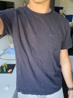 Mörkblå t-shirt från Zara - En enkel och stilren mörkblå t-shirt från Zara med rund halsringning och en bröstficka på vänster sida. Tillverkad i mjuk bomull och har en normal passform. Perfekt basplagg till garderoben.
