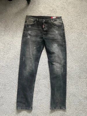 Grå slitna skinny jeans Dsquared - Säljer ett par grå skinny jeans med slitningar och tvättade detaljer. Jeansen har fem fickor, bälteshällor och knappgylf. Materialet är klassisk denim med stretch för extra komfort. Perfekta för en avslappnad och trendig look.