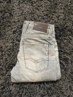 Ljusgrå slim fit jeans från Replay - Snygga ljusgrå jeans från Replay med slim fit passform och klassiska fem fickor. Jeansen har diskreta slitningar, kontrastsömmar och en liten röd detalj på bakfickan. Tillverkade i mjukt denimtyg som ger en skön känsla och modern look.