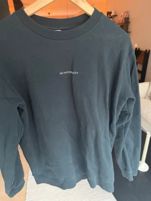 Svart sweatshirt från NN07 - Säljer en svart sweatshirt från NN07 med texten 'No Nationality' broderad på bröstet. Tröjan har rund halsringning och långa ärmar. Perfekt för en avslappnad och stilren look.