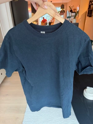 Mörkblå t-shirt från Uniqlo U - En stilren mörkblå t-shirt från Uniqlo U i storlek M. Klassisk passform med rund hals och korta ärmar. Tillverkad i mjuk bomull som känns skön mot huden. Perfekt basplagg för alla tillfällen.