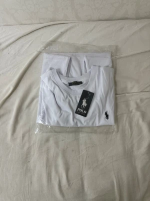 Vit t-shirt från Polo Ralph Lauren och svart - Klassisk svart/vit t-shirt från Polo Ralph Lauren med rund halsringning och den ikoniska loggan broderad på bröstet. T-shirten är i mjuk bomull och har en stilren, enkel design som passar till det mesta.