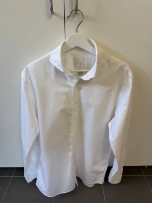 Vit skjorta från Oscar Jacobson, stl 40 - Klassisk vit skjorta från Oscar Jacobson i bomull. Skjortan har lång ärm, knappar framtill och en tidlös design som passar till många olika stilar. Perfekt för dig som gillar en clean och stilren look.