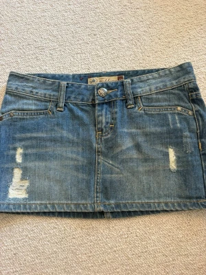 Blå jeanskjol med slitningar - Säljer en kort blå jeanskjol med slitna detaljer och klassiska fickor både fram och bak. Kjolen har bälteshällor och stängs med knapp och dragkedja. Perfekt för dig som gillar en avslappnad och trendig stil.💓