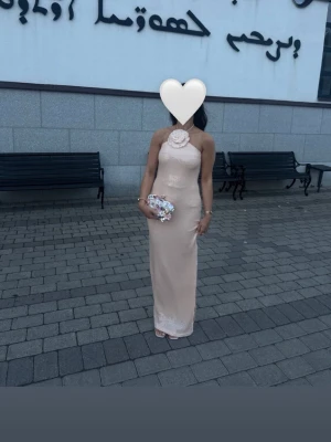 Bella Barnett klänning  - Elegant lång ljusrosa klänning med halterneck och stor blomdetalj vid halsen. Perfekt för speciella tillfällen, fester, bröllop. Storlek M men passar S. 