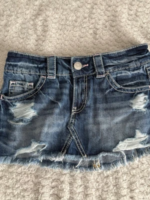 Jeanskjol från gina tricot - Säljer en jeanskjol med slitna detaljer och fransig kant. Perfekta för sommaren. Helt nya utan lapp