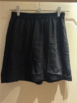 Svart kortkjol från Gina Tricot - Säljer en svart kortkjol från Gina Tricot med resår i midjan. Kjolen har en enkel och klassisk design med lätt utställd passform, perfekt att matcha med olika toppar. Materialet känns mjukt och bekvämt mot huden.