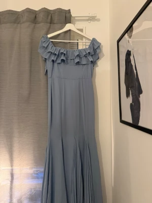 Ljusblå långklänning med volang - Superfin ljusblå långklänning med offshoulder och volangdetaljer upptill som passar perfekt till bal! Klänningen har en elegant och flowy passform med plisserad nederdel och dragkedja i ryggen. Klänningen är köpt på Bubbleroom men är från märket Goddiva. Den är i storlek S! 🩵