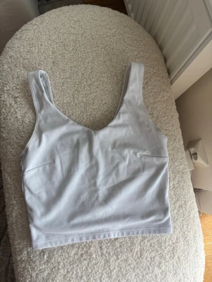 Vit croppad linnetopp - Snygg vit croppad linnetopp med breda axelband och djup rundad halsringning. Tillverkad i mjuk bomull, perfekt för varma dagar eller som layering-piece. Enkel och stilren design som passar till det mesta. Finns en fläck som syns på bilden!