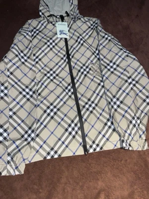 Burberry Vindjacka  Storlek L - Säljer en Burberry vindjacka i storlek L. Jackan är helt ny och endast testad, fortfarande med originaltaggar kvar. Endast plastpåsen saknas.  ✅ Detaljer:  * ✅ Märke: Burberry * ✅ Storlek: L * ✅ Färg: Beige med klassiskt Burberry-rutmönster * ✅ Skick: Helt ny, endast testad * ✅ Originaltaggar medföljer * ✅ Originalpåsen saknas * ✅ Huva med justerbar dragsko * ✅ Dragkedjestängning * ✅ Fraktas samma dag vid snabb betalning   Perfekt och stilren vindjacka med Burberrys ikoniska design. Hör av dig 