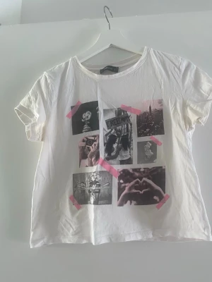 Vit t-shirt med fototryck och rosa detaljer - Vit t-shirt med flera svartvita fototryck framtill, dekorerad med rosa tejpdetaljer. T-shirten har rund hals och korta ärmar. Perfekt för dig som gillar en kreativ och ungdomlig stil. Tillverkad i mjuk bomull för skön känsla.