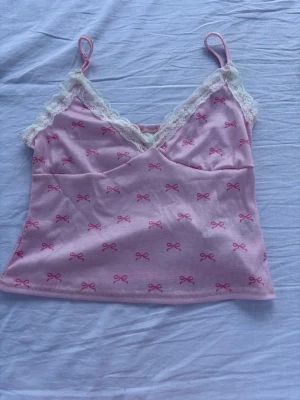 Rosa linnetopp med spets från SHEIN🎀 - Sött rosa linne från SHEIN med vit spets och rosa rosetter 🎀 Använt endast en gång och är i väldigt fint skick!  Ordinarie pris: 50 kr. - Säljer för: 25 Öppen för andra bud. Tvättlappen har lossnat, men jag har lagt med en bild på lappen bredvid så material och information syns.  Hör gärna av dig om du har frågor 💕