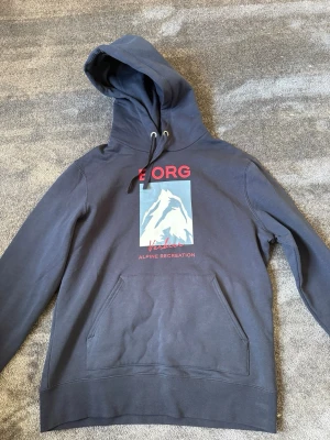 Björn borg hoodie  - Snygg mörkblå hoodie med stor huva och dragsko. Framtill finns ett tryck med texten 'BORG' och en bergsillustration i vitt och blått samt röda detaljer. Hoodien har en stor magficka och ribbade muddar vid ärmar och nederkant. Perfekt för en avslappnad stil. Storlek xl perfekt skick använd ett fåtal gånger 