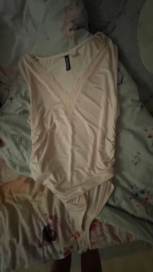 Ljusrosa body från H&M Divided - Säljer en ljusrosa body från H&M Divided i storlek L. Bodyn har djup V-ringning med spetsdetaljer och är tillverkad i ett mjukt, stretchigt material. Perfekt att styla med jeans eller kjol för en trendig look.