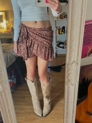 Brun blommig omlottkjol med volang - Supersöt brun omlottkjol från Only med vitt blommönster och volangkant. Kjolen har knyt i sidan och är anpassningsbar 🤎🐞