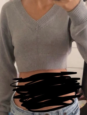 Grå cropped stickad tröja Gina Tricot - Snygg grå cropped stickad tröja från Gina Tricot med v-ringning och bred ribbad kant vid ärmslut och nederkant. Perfekt till höga jeans eller kjol. Mjuk och skön kvalitet, långärmad och enkel att styla till olika looks.