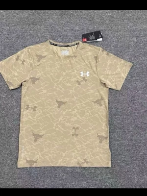 Beige camo t-shirt från Under Armour - Snygg beige t-shirt från Under Armour med camouflagemönster och korta ärmar. T-shirten har en vit logga på bröstet och är tillverkad i ett lätt och skönt material, perfekt för en avslappnad stil.