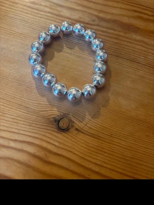 Armband med stora silverfärgade pärlor - Snyggt armband med stora, runda silverfärgade pärlor trädda på elastisk tråd. Perfekt för dig som gillar en enkel men ändå iögonfallande accessoar. Passar till många olika stilar och är lätt att matcha med andra smycken.