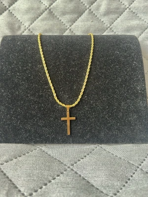 Guldhalsband med korshänge - Snyggt halsband i guldfärgad stål med ett stilrent korshänge. Kedjan har tvinnad design och ett smidigt lås. Perfekt accessoar för dig som gillar klassiska och tidlösa smycken med en modern touch. 50cm. Checka in min profil för passande armband.