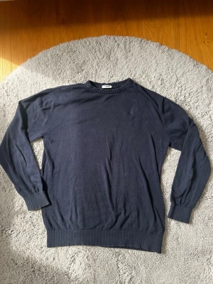 Mörkblå stickad tröja - En enkel och stilren mörkblå stickad tröja med rund halsringning och ribbade muddar vid ärmslut och nederkant. Tröjan är i storlek 158/164. Den ör i väldigt bra skick! Inga hål eller liknande.