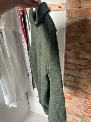 Mörkgrön stickad tröja med halvzip - Mysig mörkgrön stickad tröja från Casual Friday med hög krage och halv dragkedja framtill. Tröjan har lång ärm och är gjord i ett mjukt, fluffigt material som känns riktigt skönt mot huden. 