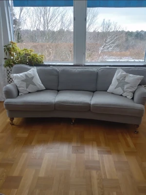 Mio soffa 3-sits grå tyg - Mio oxfordsoffa 3-sits i grått tyg. Soffan har tre sittdynor och tre ryggkuddar samt rundade armstöd. Benen är i trä med hjul framtill. Använd, i gott skick. Säljer för att vi flyttar till mindre boende.