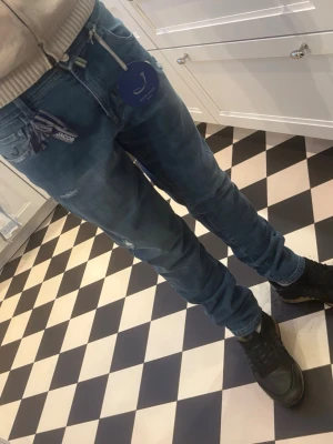 Blå slim fit jeans från Jacob Cohen - Snygga blå slim fit jeans från Jacob Cohen med klassisk femficksmodell och diskreta slitningar. Jeansen har dragkedja, vita och blå detaljer vid fickorna samt ett litet broderat märke. Materialet är stretchigt för extra komfort. Helt nya aldrig använda säljer för att de är för små. 2800 nya. Vill bli av med de behöver lite pengar. Kom med frågor.