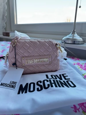 Love Moschino Qulited PU Cipria Rosa - Love Moschino JC4064PP1HLA0608 Supersnygg ljusrosa handväska från Love Moschino med quiltat mönster och guldfärgade detaljer.  Kommer med originalpåse och tagg. Oanvänd