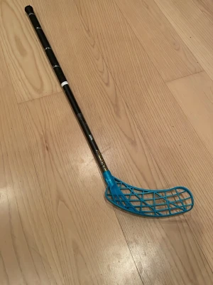 Zone innebandyklubba svart/blå - Säljer en kapad innebandyklubba från Zone med svart skaft och blått air one blad. Skaftet har hexagonmönster och texten 'Power' i guld. Perfekt för dig som vill ha bra kontroll och stil på planen. Släpptes hösten 2025 längd=83cm. Hör av er vid frågor eller funderingar💯 KÖP BARA VIA POSTNORD.Perfetk för dig som vill ha en lätt klubba som inte går sönder. Bladet kostar 350 nytt också.