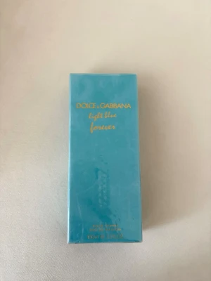 Dolce & Gabbana Light Blue Forever - Fräsch parfym från Dolce & Gabbana, Light Blue Forever. Kommer i en snygg, rektangulär turkosblå kartong med guldfärgad text. Förpackningen är stilren och modern, perfekt för dig som gillar exklusiva dofter och vill ha något som sticker ut i badrumsskåpet.