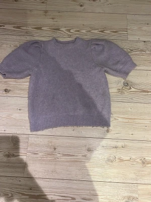 Ljuslila stickad tröja med puffärm - Söt ljuslila stickad tröja med puffärmar och ribbade muddar vid ärmslut och nederkant. Tröjan har en rund halsringning och är gjord i ett mjukt, mysigt material. Perfekt för dig som gillar en enkel men trendig look.