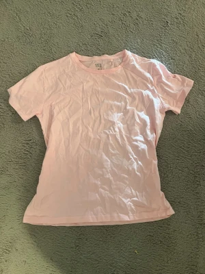 Ljusrosa basic t-shirt från 157 - En enkel och stilren ljusrosa t-shirt från 157. T-shirten har rund halsringning och korta ärmar, perfekt för en avslappnad look. Tillverkad i 100% mjuk bomull som känns skön mot huden.