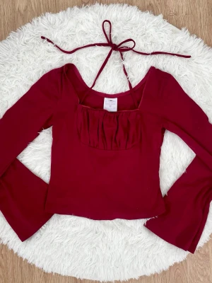 Mörkröd långärmad topp med knyt - Trendig mörkröd långärmad topp med snygg knytning i nacken och rynkad detalj framtill. Storlek: S, passar 34-36.