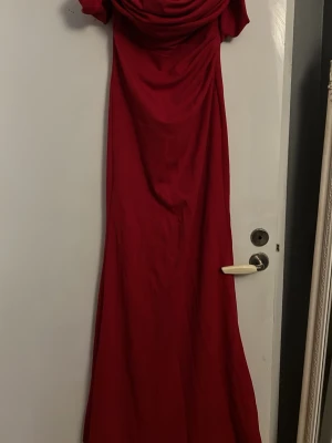 Röd långklänning med draperad topp - Säljer en elegant röd långklänning med offshoulder och draperad överdel. Klänningen har en figurnära passform och faller snyggt längs kroppen. Perfekt för dig som vill sticka ut med en klassisk och stilren look. Ändats använd en gång , pris kan diskuteras 