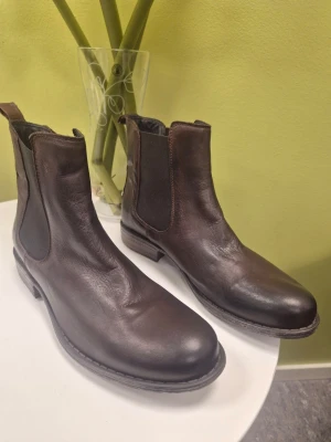 Rosa Negra chokladbruna Chelsea boots i skinn 41 - Snygga mörkbruna Chelsea boots i äkta skinn med klassisk rund tå och elastiska paneler på sidorna. Perfekt för dig som gillar stilrena och tidlösa skor. Dragflik bak för enkel påtagning och låg klack för bekväm känsla hela dagen.
