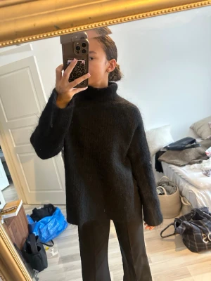 Svart stickad polotröja i mohairmix - Mysig svart stickad polotröja med lös passform och höga ärmslut. Tröjan är gjord i en fluffig mohairmix som ger en lyxig känsla och extra värme. Perfekt för lager-på-lager och enkel att styla till olika outfits.