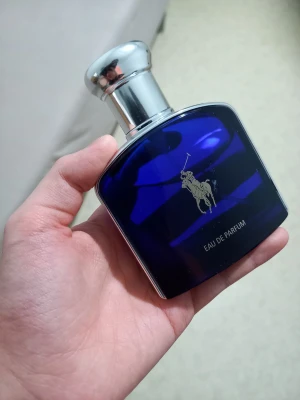 Ralph Lauren blå Eau de Parfum - Snygg parfymflaska från Ralph Lauren i djupblått glas med silverfärgat lock och den klassiska polospelaren i silver på framsidan. Flaskan har en modern, stilren form och känns lyxig att hålla i handen. Perfekt för dig som gillar exklusiva dofter.