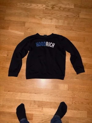 Svart tröja från Hoodrich - Svart långärmad tröja från Hoodrich med tryckt logga i blått och vitt framtill. Klassisk rund halsringning och normal passform. Perfekt till jeans eller joggers för en avslappnad look. ‼️‼️XL BARN STORLEK PASSAR PERFEKT PÅ S VUXEN!‼️‼️