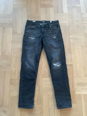 J&J Svarta Jeans Slitningar - Ett par riktigt snygga jeans från märket Jack & Jones. De är svarta och har snygga slitningar. Storlek är W28 L 30, om du har frågor angående storlek hör gärna av dig!  * Fraktas samma dag som köp (gäller vid köp innan kl 18.00).