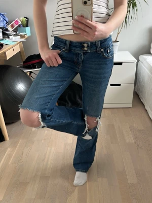 Lågmidjade bootcut jeans med hål i knäna - Säljer ett par blå bootcut/flare jeans med stora slitningar vid knäna från lager 157. Lågmidjade, har två knappar vid midjebandet och är utsvängda mot fötterna. Var jätte populära när de kom och är slutsålda online och nästan överallt, ”Paris core”. Storlek XS och är i short lenght (passar mig som är 166 cm) Mycket bra skick, endast använda 2-3 gånger. Ordinarepris 400 kr. 