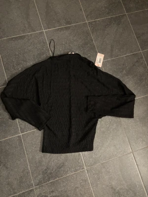 Svart långärmad topp från Nelly - TRYCK EJ PÅ KÖP DIREKT!!Trendig svart långärmad topp från nelly med lätt ribbad struktur. Toppen har en hög hals och är tillverkad i ett mjukt, stretchigt material som sitter snyggt på kroppen. Perfekt att styla med både jeans och kjol.