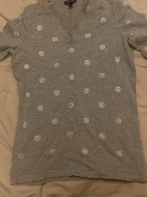 Grå prickig v-ringad topp - Grå topp från Tommy hilfiger som har vita bollar över hela tröjan. Tröjan är som ny och knappt använd och är köpt för 300kr pris kan diskuteras. Hör gärna av dig om du är intresserad!! 