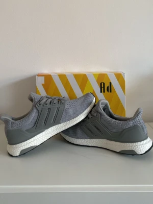 Grå sneakers - Snygga grå sneakers med stickad ovandel och klassiska tre ränder på sidan. Skorna har en vit sula för extra komfort och grå detaljer runt hälen. Perfekta för dig som gillar stilrena och bekväma sneakers.