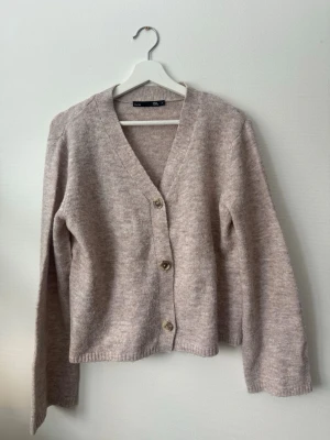 Ljusbeige kofta med knappar - Säljer en ljusbeige kofta med v-ringning och tre knappar framtill från Lager 157. Koftan har lång ärm och är stickad i ett mjukt material som känns skönt mot huden. Perfekt att slänga över en t-shirt eller topp. I storlek S.