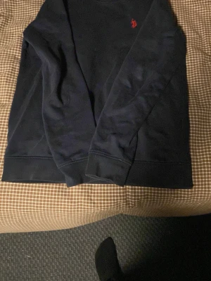 Mörkblå sweatshirt från Ralph Lauren - Mörkblå sweatshirt från Ralph Lauren med klassisk röd logga broderad på bröstet. Tröjan har rund halsringning, långa ärmar och ribbade muddar vid ärmslut och nederkant. Perfekt för en avslappnad och stilren look.