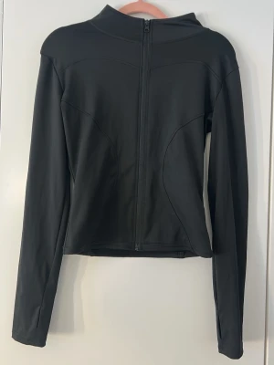 Svart träningströja med  zip   - Snygg svart zip-träningströja, figurnära passform. Tröjan har långa ärmar och dragkedja framtill. Tillverkad i ett stretchigt material som ger en sportig look. Perfekt att matcha med jeans eller tights.