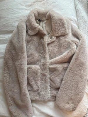 Beige teddyjacka från H&M - Supermjuk teddyjacka i beige från H&M med bred krage och stora fickor framtill. Jackan har en oversized look och stängs med knappar. Perfekt för dig som vill ha en mysig och trendig jacka till hösten eller vintern.